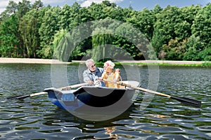 Aged wife and husband holding paddles having nice river trip in boat photo