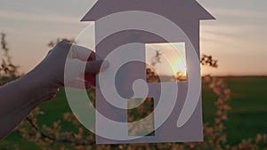 holding a paper house at sunset, a mortgage loan to a young family, a ray of sunlight shining through the window