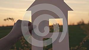 holding a paper house at sunset, a mortgage loan to a young family, a ray of sunlight shining through the window