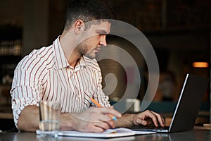 Holding pen and serching some information. Adult man sits in cafe at daytime and using the laptop for the remote work