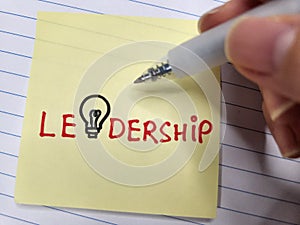 Holding a pen with a sticky note showing the word Leadership