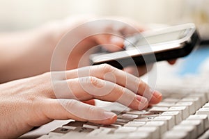 Holding phone hand typing computer keyboard