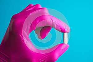 Holding pill capsule drugs in hand pink latex glove