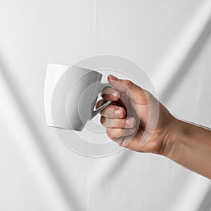 Holding a plain white ceramic mug against a soft white fabric