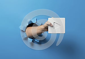 Holding Play Button Through Torn Blue Paper Background