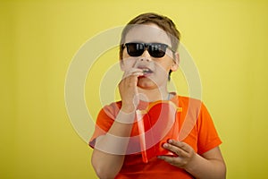 Holding a portion of french fries in his hand, the child takes a bite. Isolated on a yellow background. The boy eats
