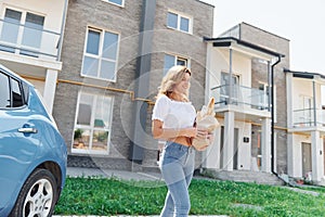 Holding products in bag. Young woman in casual clothes with her electromobile outdoors at daytime