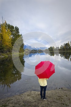 Holding a red umbrella by the river