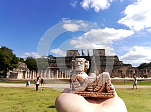 Holding a small Chac-Mool statue on the palm of the hand against the background with tourists and the Temple of Warriors in Mexico photo
