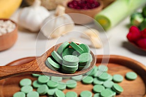 Holding spoon of prebiotic pills near table with food, closeup