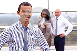 Holding a tablet, a young handsome black businessman is standing outside of a business building, confidently looking