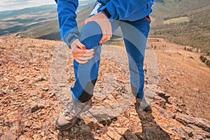 Holding on to the knee joint, suffering from acute pain. Concept of injury of meniscus during a hike in the highlands