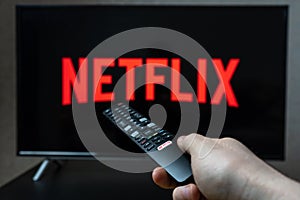 Holding TV remote controller with Netflix logo.