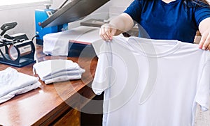 holding white shirts behind a sublimation or screen printing machine for t-shirts.