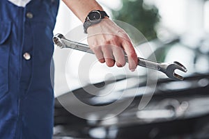 Holding wrench. Woman repairer is on her work. Indoors at car shop