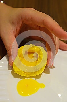 Holding Yellow Custard Bun with the filling oozing out