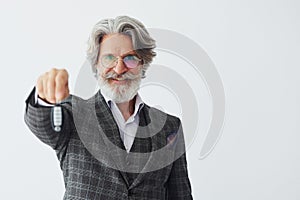 Holds car keys in hand. Senior stylish modern man with grey hair and beard indoors