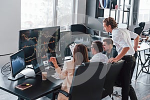 Holds document in hands. Team of stockbrokers works in modern office with many display screens