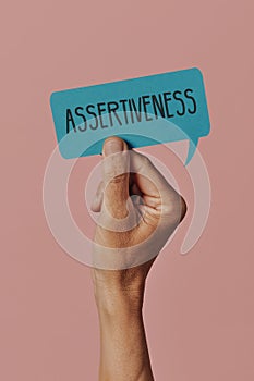 Holds a sign with the text assertiveness