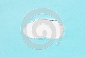 Hole in blue paper on white background. Pastel color paper with torn edges