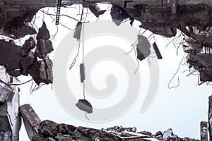 A hole in the body of a building with a pile of construction debris and concrete fragments hanging on the rebar against photo