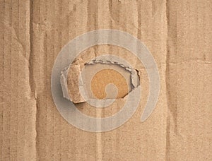 Hole in brown cardboard paper with torn and curved edges