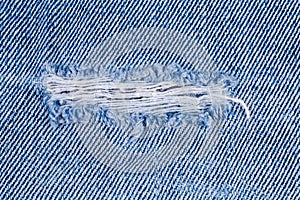 Hole on denim jeans with frayed threads close-up