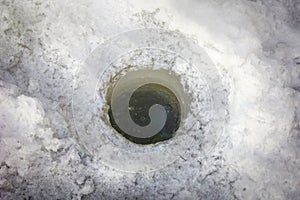 A hole for fishing on the ice surface of a frozen lake close-up