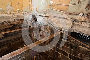 Hole in floorboards during home renovation showing rotting damaged joists