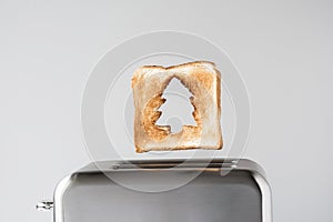 Hole in a form of christmas tree on roasted toast bread popping up of stainless steel retro toaster for breakfast preparation.