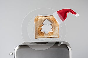 Hole in a form of christmas tree on roasted toast bread with red Santa Claus hat popping up of retro toaster for breakfast prepara