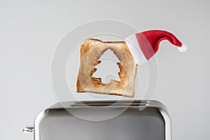 Hole in a form of christmas tree on roasted toast bread with red Santa Claus hat popping up of retro toaster for breakfast prepara