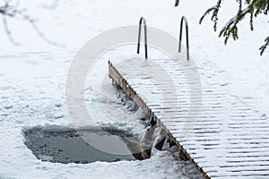 Hole in a frozen lake with wooden pier covered in snow