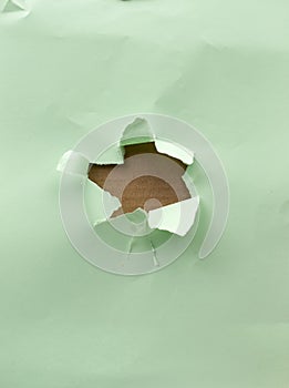 Hole in green paper with torn and curved edges