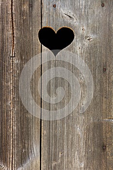 A hole in heart shape in an old wooden door