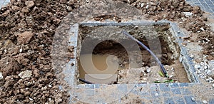 Hole for installation pillar or pole on cement ground with water and black wire cable