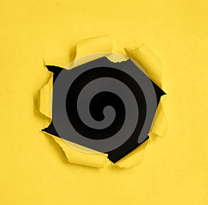 Hole in the paper with torn sides over yellow background