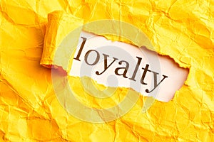 Hole on the paper with torn yellow sides inside written loyalty