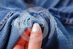 Hole and Threads on Denim Jeans. Ripped Destroyed Torn Blue jeans background. Close up blue jean texture