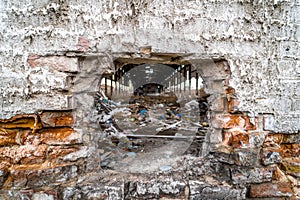 Hole in a wall into the old destroyed factory with a lot of broken debris inside