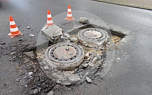 Holes and damage on an asphalt road, secured by red and white shut-off cones because of the risk of accidents