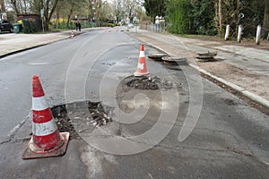 Holes and damage on an asphalt road, secured by red and white shut-off cones because of the risk of accidents