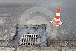 Holes and damage on an asphalt road, secured by red and white shut-off cones because of the risk of accidents