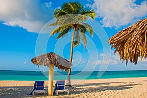 Holguin, Cuba, Playa Esmeralda. Umbrella and two lounge chairs around palm trees. Tropical beach on the Caribbean sea. Paradise la