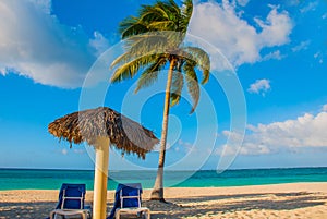 Holguin, Cuba, Playa Esmeralda. Umbrella and two lounge chairs around palm trees. Tropical beach on the Caribbean sea. Paradise la