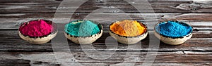 Holi festival. Colored holi powders in a bowl on a dark rustic wooden table, banner. Selective focus