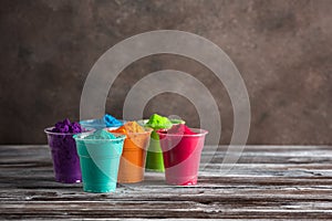 Holi festival.Colorful holi powders in plastic cups on a wooden old table. Selective focus