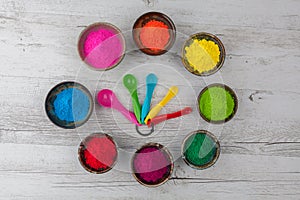 Holi powder in cups arranged in circle with measuring spoons