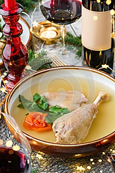 Holiday aspic or galantine with chicken in plate on wooden table served with plates, glasses, bottle of wine, candles, fir