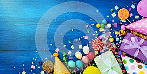 Holiday background with balloons, gift boxes and confetti. Birthday and party supplies on blue table top view. Banner format